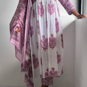 A woman wearing a rosewood pink Kalamkari set with a gathered waist tunic, printed bottoms, and a lightweight dupatta, posing against a white wall.