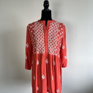 Coral embroidered short kurti with intricate white floral patterns, displayed on a black mannequin against a plain background.