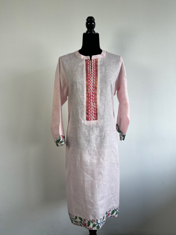 Pink linen kurti on a mannequin, featuring a white front panel with embroidered detailing and floral-printed cuffs.