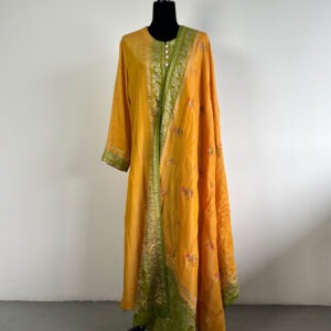 Mustard and green embroidered silk suit set on a black mannequin, featuring intricate embroidery, a contrasting border, and a matching dupatta.