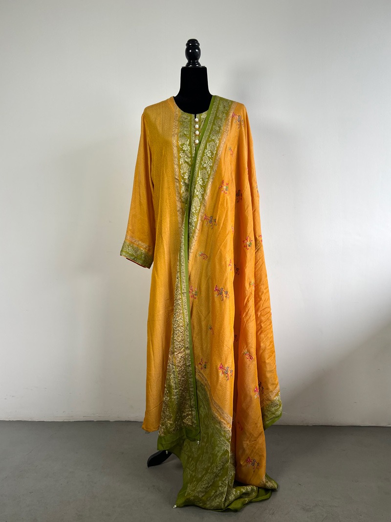 Mustard and green embroidered silk suit set on a black mannequin, featuring intricate embroidery, a contrasting border, and a matching dupatta.