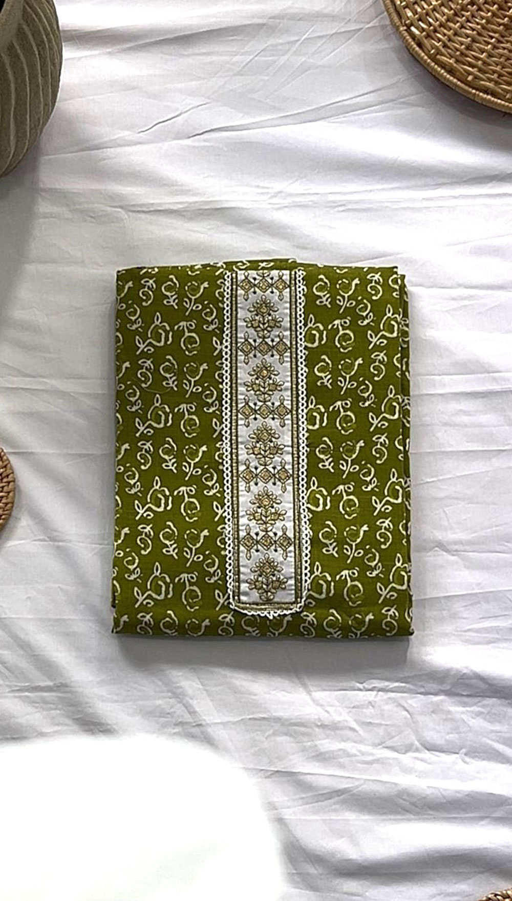 Green unstitched material with white floral embroidery and an intricately embroidered front panel, laid flat on white fabric.