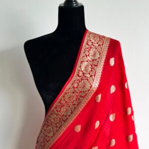 Red Banarasi-style dupatta with antique gold floral border and woven motifs, finished with red tassels, draped on a black mannequin.