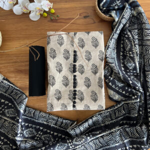 Unstitched 3-piece material set with beige floral printed top, plain navy pant material, and indigo patterned dupatta with tassels laid flat on a wooden table.