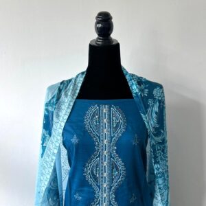 Teal unstitched 3-piece material set displayed on mannequin showing embroidered neckline and printed blue dupatta.