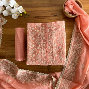Peach unstitched 3-piece material set laid on a flat table showing floral embroidered top, plain pant material, and lace-detailed matching dupatta.