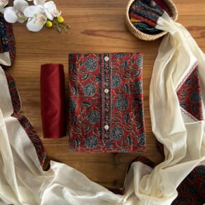 Brick red unstitched 3-piece set with floral top, off-white dupatta, and pant laid on table.