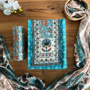 Sea blue block print unstitched 3-piece material set laid on a wooden table with folded top fabric, pant piece rolled neatly, and matching printed dupatta placed beside it.