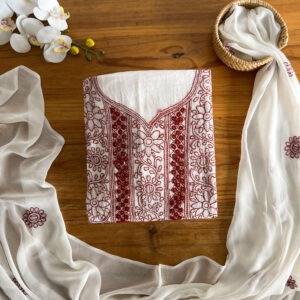 Plum embroidered unstitched three-piece material set laid flat on a wooden table with sheer dupatta and plain pant fabric